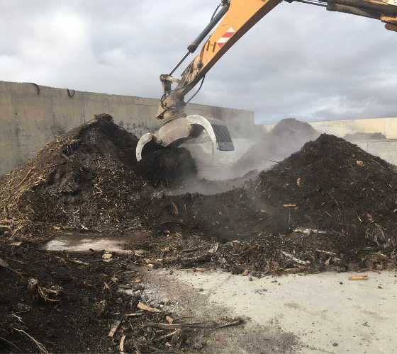 Montaña de compost y una pinza excavadora está trabajando sobre ella