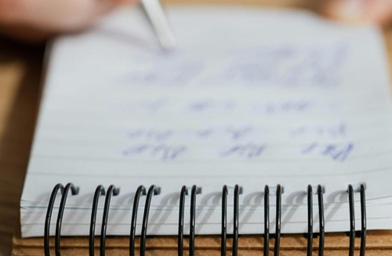 Mano con un bolígrafo plateado escribiendo sobre un cuarderno de anillas