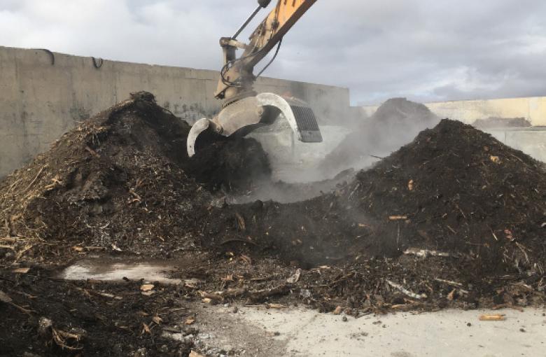Montaña de compost y una pinza excavadora está trabajando sobre ella