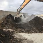 Montaña de compost y una pinza excavadora está trabajando sobre ella